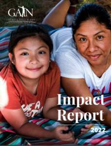 GAIN Impact Report 2022. Background image is of a smiling Latina woman and young girl laying on top of a colorful towel in the grass.