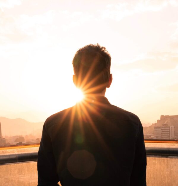 A man in silhouette with his back to the camera. Sunlight is glinting from past his shoulder.